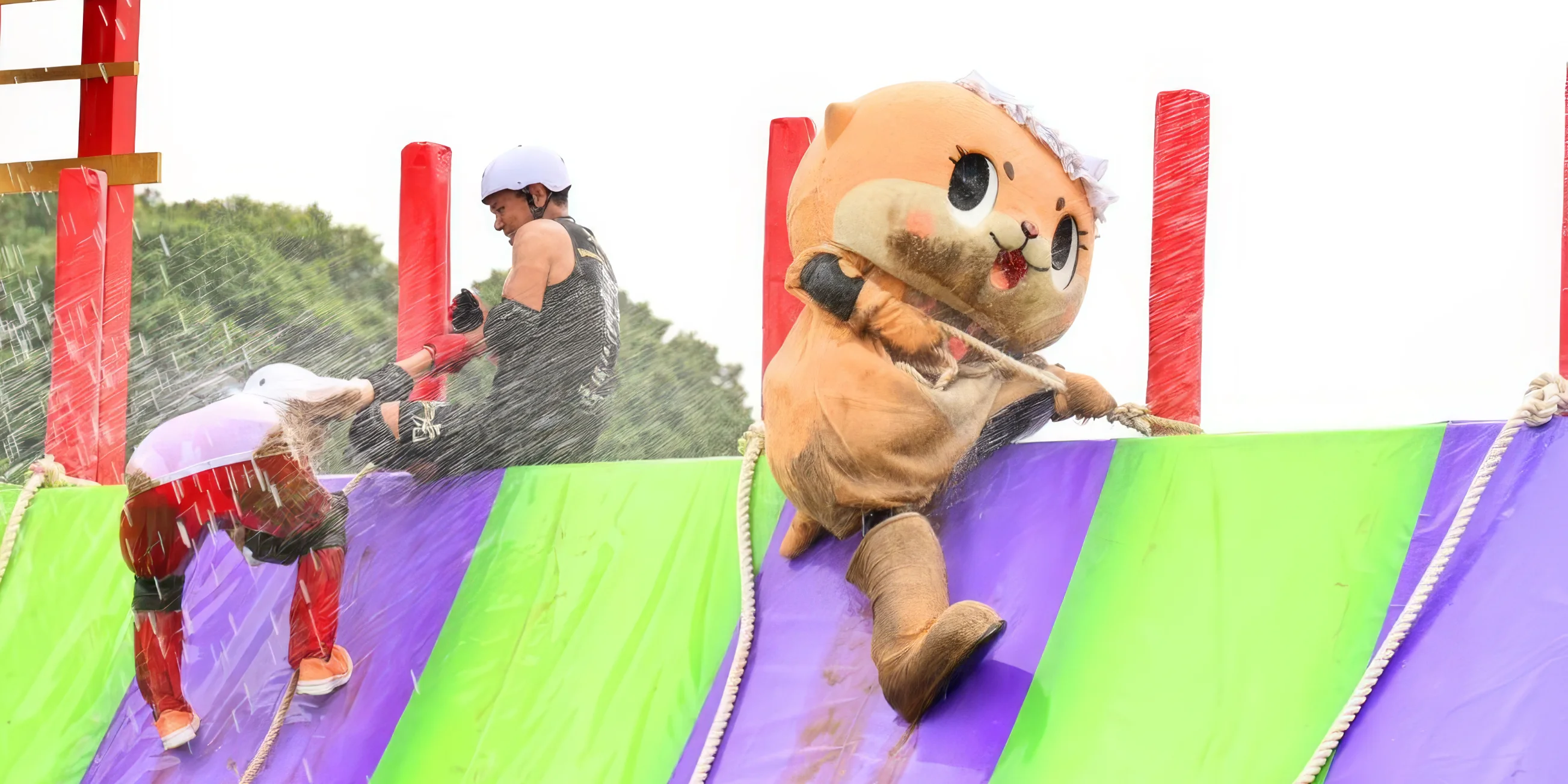 A giant otter mascot climbs over the top of a tall slippery slope